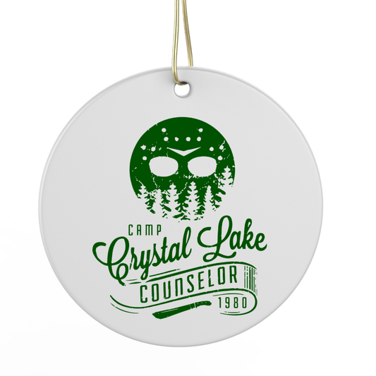A white circular ornament with a green design featuring a stylized face and trees, along with the text "Camp Crystal Lake Counselor 1980".